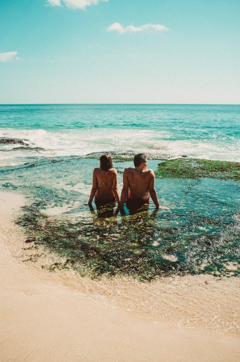 a man and woman sitting on a beach in the water