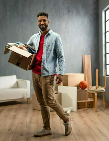 Happy young man holding packing boxes moving home, looking at camera, new living concept.