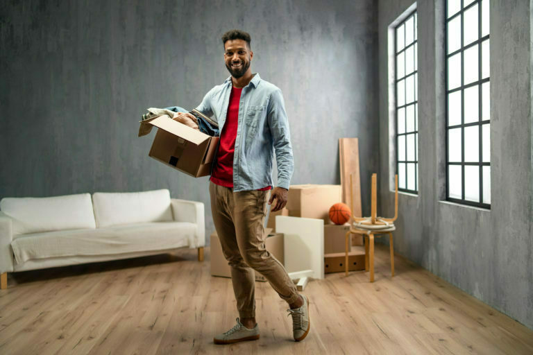 Happy young man holding packing boxes moving home, looking at camera, new living concept.