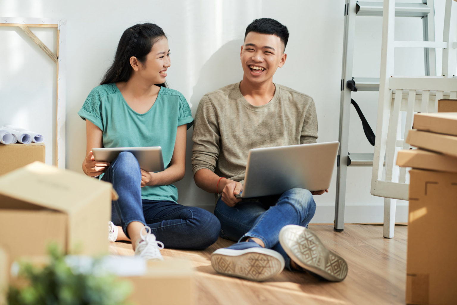 Laughing couple with gadgets in new apartment